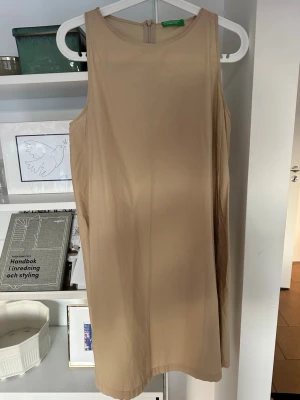 Beige ärmlös klänning. - Snygg beige ärmlös klänning med rund halsringning och A-linjeform.. Klänningen är kort och har en lätt och luftig känsla, perfekt för varma dagar. Stängs med dragkedja i ryggen. Fickor. Enkel och stilren design som är lätt att matcha.