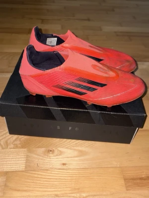 F50 fotbollsskor - Säljer ett par röda Adidas F50 fotbollsskor med svarta detaljer och strömlinjeformad design. Skorna har låg profil, utan snörning och är tillverkade i syntetmaterial för lätt vikt och bra bollkontroll. Perfekta för snabba spelare som vill sticka ut på planen.