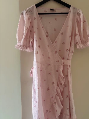 Ljusrosa klänning Gina Tricot - Supersöt ljusrosa klänning från Gina Tricot med små blommor, puffärmar och volangkant. Klänningen har knyt i midjan och v-ringning. Perfekt för sommarens alla tillfällen! Använd endast en gång. 
