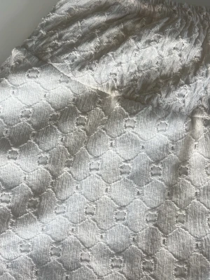 Vit kjol med strukturmönster - Säljer en vit kjol med elastisk midja och snyggt strukturmönster i tyget. Kjolen har en lätt A-linjeform och är tillverkad i ett tyg med diskret glans och textur. Perfekt för dig som gillar stilrena och trendiga plagg.