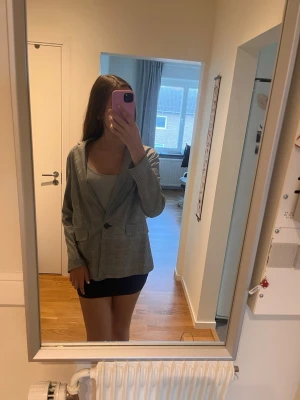Grå rutig oversized kavaj - Snygg grå kavaj med rutigt mönster och oversized passform. Kavajen har en knapp framtill, två fickor och klassisk krage. Perfekt att styla med kjol eller jeans för en trendig look.