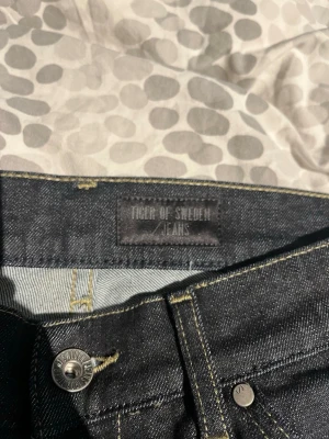 Mörkblå jeans från Tiger of Sweden - Snygga mörkblå jeans från Tiger of Sweden i klassisk rak modell. Jeansen har fem fickor, silverfärgade detaljer och är tillverkade i ett slitstarkt denimtyg. Perfekta för dig som gillar stilrena och tidlösa jeans. Slimjeans/raka