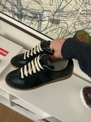 Maison Margiela GAT - Strl 42 (Black/Gum) - Säljer ett par riktigt snygga sneakers i storlek 42. Använda sparsamt och i fint skick. Passar perfekt till både vardag och en mer uppklädd outfit.   Box medföljer om du vill ha den.  Extra svarta skosnören ingår, utöver de vita som sitter på skorna.  Skicka gärna meddelande om du har frågor eller vill ha fler bilder. 😊