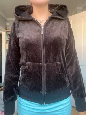 Mjuk brun velourhoodie med dragkedja - Säljer en brun hoodie i mjuk velour med dragkedja framtill och stor huva. Hoodien har fickor på magen och ribbade muddar vid ärmar och nederkant. Perfekt för en chill och avslappnad stil.