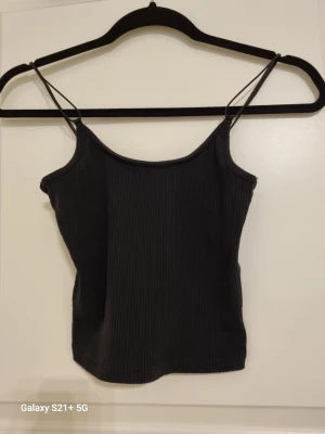 Svart ribbad linnetopp XS/S - Säljer en svart ribbad linnetopp med smala axelband. Toppen har en enkel och stilren design som passar perfekt till många olika outfits. Materialet är mjukt och stretchigt för en bekväm passform.