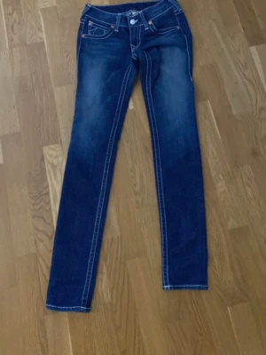 Mörkblå raka jeans med kontrastsömmar - Snygga mörkblå jeans med raka ben och tydliga vita kontrastsömmar. Jeansen har klassisk femficksmodell och detaljerade sömmar på fickorna. Materialet är denim i bomull med lätt tvättad look för en avslappnad stil.