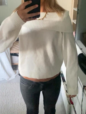 Vit off shoulder stickad tröja - Vit stickad tröja med off shoulder-design och bred ribbad kant upptill. Tröjan har långa ärmar och ribbade muddar vid ärmslut och nederkant. Perfekt för dig som vill ha en trendig och mysig look.