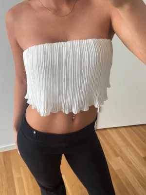 Vit plisserad bandeau tubtopp - Säljer en vit bandeau tubtopp med plisserad struktur och vågig kant nertill. 