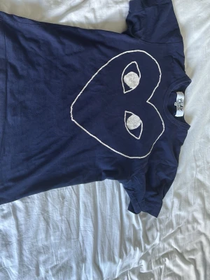 Mörkblå t-shirt Comme des Garçons - Snygg mörkblå t-shirt från Comme des Garçons Play med det ikoniska hjärtat med ögon tryckt på bröstet. T-shirten har rund hals och är tillverkad i mjuk bomull. Perfekt för dig som gillar streetstyle och vill sticka ut med en cool design. Nypris:1350 mitt pris är 550. Sitter lite kort på mig då jag är 181 rekommenderas för folk som är mellan 175-165