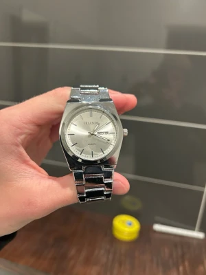 Silverfärgad klocka med metallarmband - Stilren klocka med rund urtavla i silver och matchande metallarmband. Urtavlan har tydliga markeringar och dag- och datumvisning. Klassisk design som passar till många olika stilar.