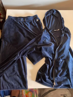 Mörkblått loungewear-set från Zink - Mysigt mörkblått loungewear-set från Zink i mjukt material. Setet består av ett par byxor med resår i midjan och en matchande hoodie med dragkedja och huva. Perfekt för chill dagar hemma eller när du vill vara bekvämt klädd.