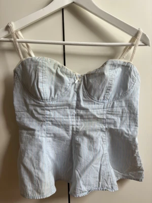 Ljusblå randig topp från Zara - Supersöt ljusblå sommar topp från Zara med tunna vita ränder och spetsdetaljer på axelbanden. Toppen har en liten rosett framtill och bygel för extra form. 