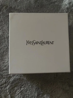 Svart bälte från Yves Saint Laurent - Snyggt svart bälte från Yves Saint Laurent med klassisk silverfärgad YSL-logga på spännet. Skärpet är gjort i slätt skinn och har en stilren, rektangulär metallspänne. Perfekt accessoar för att lyfta vilken outfit som helst. Boxen och allt ingår. Pris kan diskuteras i DM.