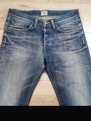 00s Archive Denim Japan - Säljer ett par blå jeans från Edwin med rak passform och slitna detaljer. Riktigt feta retro jeans i japan denim stil. Jeansen har klassiska bakfickor med broderi och en patch med Edwin-loggan i midjan. Materialet är denim i bomull och färgen är tvättad blå med tydliga slitningar. Byxorna är i storlek 33/34 men passar 32 i midjan. 