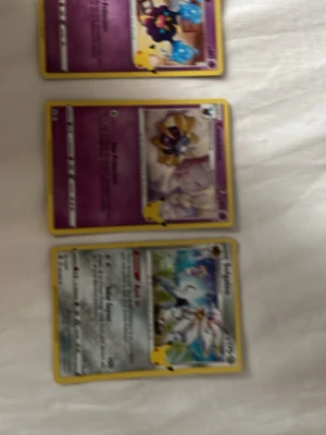 Tre Pokémonkort med Pikachu-motiv - Säljer tre Pokémonkort med gul ram och Pikachu-motiv i hörnet. Korten har färgstarka illustrationer och text på framsidan, samt den klassiska blå baksidan med Pokéboll. Perfekt för samlare eller Pokémonfans.