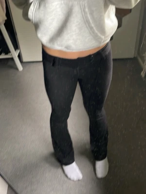 Svarta utsvängda kostymbyxor - Säljer ett par svarta kostymbyxor med utsvängda ben och hög midja. Byxorna har bälteshällor och en klassisk, stilren look. Perfekta för dig som gillar en trendig och clean stil. Materialet ser ut att vara mjukt och följsamt.