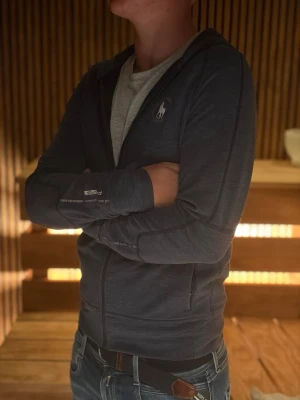 Mörkblå hoodie med dragkedja - Snygg mörkblå hoodie från Polo Ralph Lauren med dragkedja framtill och klassisk vit logga på bröstet. Hoodien har huva, långa ärmar och ribbade muddar. Perfekt för en avslappnad och stilren look. Det är en S men är liten i storleken. 