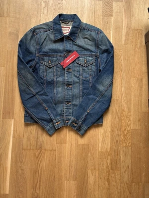 Crocker jeansjacka  -  Helt ny Snygg blå jeansjacka från crocker med klassisk rak passform och kontrastsömmar. Jackan har två bröstfickor med lock och knapp, samt knappar framtill. 