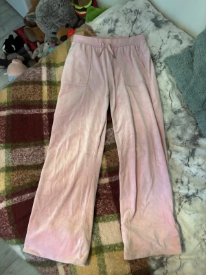 Rosa velourbyxor Juicy Couture - Säljer ett par ljusrosa mjukisbyxor från Juicy Couture i mjuk velour. Byxorna har raka ben, dragsko i midjan och två framfickor. Perfekta för en chill och avslappnad stil. Två backfickor med knappar, slitna i skrevet