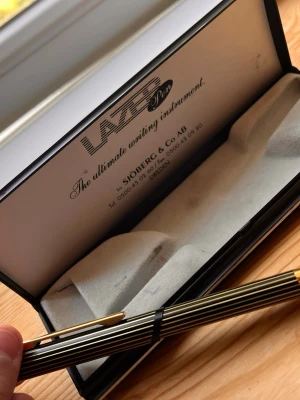 Lazer Pen randig bläckpenna i etui - Snygg randig bläckpenna från Lazer Pen i svart och guld med metallisk finish. Pennan levereras i ett stilrent svart och grått etui med mjuk insida. Perfekt för dig som gillar att skriva med stil och vill ha en penna som sticker ut på skrivbordet.
