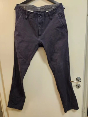 Dockers mörkblå byxor - Byxorna har en modern passform som smalnar av mot anklarna, vilket ger en stilren silhuett. De är utrustade med klassiska fickor fram och bak, samt hällor för bälte. En diskret logotyp är placerad baktill.  Nytvättade med parfymfritt tvättmedel.  Storlek W32 L32