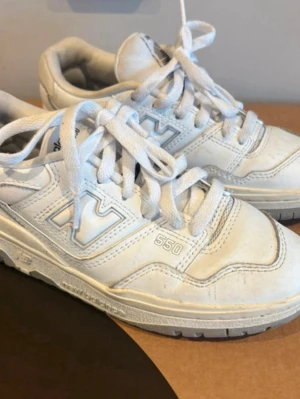 Vita New Balance 550 sneakers - Säljer ett par klassiska vita New Balance 550 sneakers med lågt skaft. Skorna har en chunky sula, tydliga NB-loggor på sidan och tåparti i läder. Perfekta för dig som gillar retrostil och streetwear.