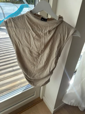 Beige ärmlös linnetopp - Säljer en enkel och stilren beige linnetopp med hög hals och ärmlös design. Toppen har en loose passform och är tillverkad i mjukt bomullsmaterial. Perfekt att matcha med jeans eller kjol för en clean look. Den har fläck som ja visa på en av bilderna