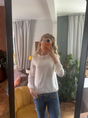 Vit blus med spetsdetaljer - Säljer en vit blus med långärmad modell och snygga spetsdetaljer upptill. Blusen har rund halsringning och ett lätt, luftigt tyg som ger en romantisk vibe. Perfekt att styla med jeans eller kjol för en trendig look.