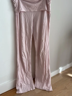 Ljusrosa leggings från Gina Tricot - Säljer ett par ljusrosa leggings från Gina Tricot i mjukt stretchigt material. De har utsvängda ben och hög midja, perfekta för en avslappnad och trendig look. Passar dig som gillar bekväma och snygga byxor i en feminin färg. De har några fläckar som man knappt märker