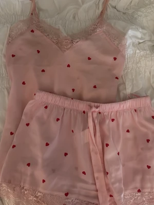 Satin pyjamasset - Supersött pyjamasset från Anna Field i ljusrosa med små röda hjärtan. Köptes 2023 och aldrig kommit till användning. Shortsen är i XS men vet inte om tröjan är för lappen är borttogen men antar det!💕💕