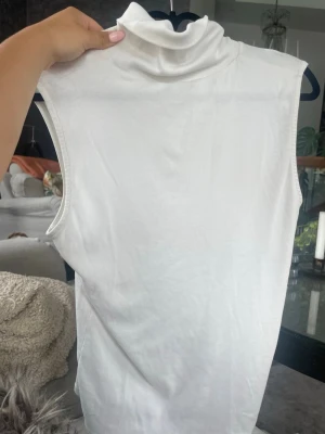 Vit ribbad ärmlös polotopp - Säljer en stilren vit ärmlös polotopp i ribbat material från Lindex, 🥹köpt på loppis som vanligt ah🥰