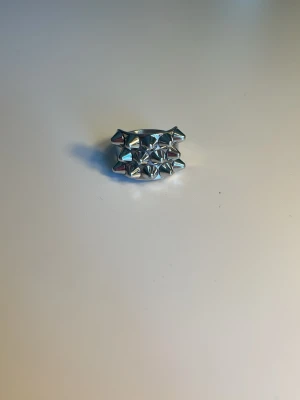 Silvrig ring med nitar - Cool ring i silverfärgad metall med flera små pyramidformade nitar på ovansidan. Ringen har en bred, slät ringbas och en edgy, modern design som sticker ut. Perfekt för dig som gillar statement-smycken och vill addera lite attityd till din stil. ⚠️pris kan diskuteras ⚠️