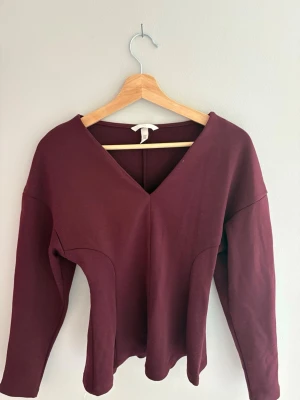 Vinröd långärmad topp med v-ringning - Snygg vinröd topp med v-ringning och långa ärmar. Modellen har en figurnära passform och är tillverkad i ett mjukt bomullstyg. Perfekt att styla med jeans eller kjol för en trendig look. Använd endast en gång. Skriv privat för mer information. 
