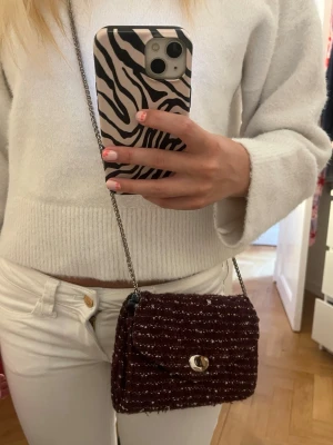 Vinröd axelremsväska ifrån Beck söndergaard - Snygg vinröd handväska i tweedmaterial med silverfärgad kedjerem och vridlås framtill. Väskan har en kompakt, rektangulär form och ett elegant mönster i vitt och vinrött. Vridlåset är lite missfärgat men förutom det så är väskan i bra form! Har köpt här på plick men bara andvännt några ggr💗