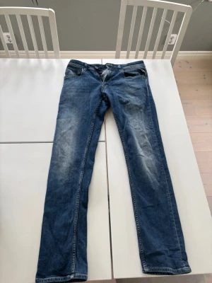 Blå raka jeans med slitningar - Säljer ett par klassiska blå jeans med raka ben och snygga slitningar på framsidan. Läng 32