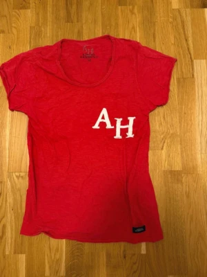 Röd t-shirt med vita bokstäver Adrian Hammond - Röd t-shirt med rund halsringning och vita bokstäver 'AH' på bröstet. Kortärmad modell i mjukt material, perfekt för en avslappnad stil. Adrian Hammond medium