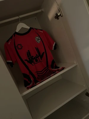 Rosa fotbollströja med nummer 10 - Snygg rosa fotbollströja med svarta och vita detaljer. Framsidan har coolt tryck och klubbmärke, medan baksidan har texten 'TOTO' och siffran 10. Tröjan har korta ärmar och sportig passform, perfekt för match eller träning.
