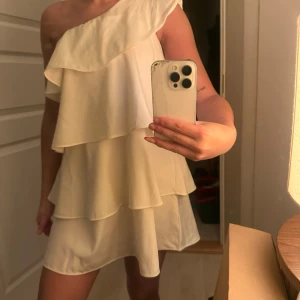 Gul volangklänning - Säljer en superfin gul kortklänning med oneshoulder och dubbla volanglager. Klänningen har en luftig passform och är perfekt för sommarens alla tillfällen. 