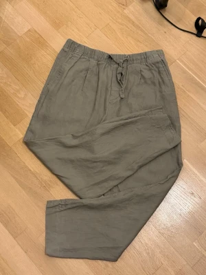 Gröna  linnebyxor - Snygga grå linnebyxor med avslappnad passform och elastisk midja med dragsko. Byxorna har raka ben och sidfickor, perfekta för en chill och stilren look. Materialet är svalt och luftigt linne.