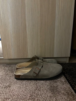 Birkenstock Boston - Säljer ett par snygga Birkenstock Boston i mocka med justerbart spänne på ovansidan. De har en klassisk slip-in design och mjuk innersula för extra komfort. Perfekta för dig som gillar stilrena och bekväma skor.