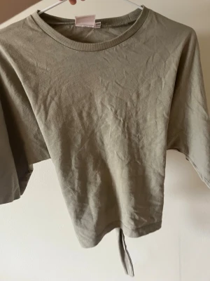 Beige croppad topp med knyt - Säljer en beige croppad topp i bomull med rund halsringning och korta ärmar. Toppen har en snygg knyt-detalj baktill som ger en trendig look. Perfekt att styla med höga jeans eller kjol.