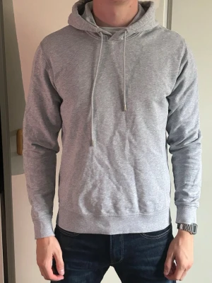 Ljusgrå hoodie från ASKET - Säljer en stilren ljusgrå hoodie från ASKET. Hoodien har huva med dragsko, långa ärmar och ribbade muddar. Tillverkad i mjuk bomullsblandning som känns skön mot huden. Perfekt för en avslappnad look.