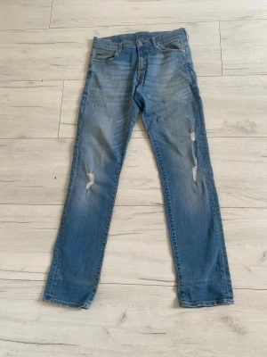 G star RAW  slim fit jeans junior stl 164 - G Star Raw jeans med slitningar på låren och knäna. Jeansen har klassisk femficksmodellm och dragkedjegylf. Materialet är denim med lätt stretch för skön passform. Perfekta för en avslappnad och trendig look. Storlek 164 ( 14 år)