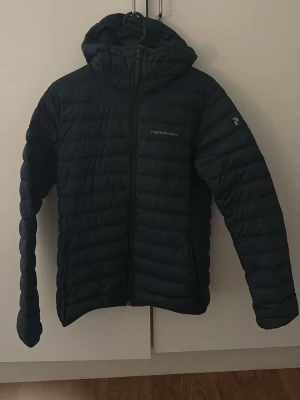 Svart dunjacka Peak Performance S - Säljer en svart dunjacka från Peak Performance i storlek S. Jackan har huva, dragkedja framtill och diskret logga på bröstet samt ärmen. Lätt och smidig modell med quiltad design, perfekt för kalla vinterdagar.