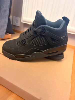 Nike Jordan 4 Retro Black Cat sneakers stl 42 - Nike Jordan Black Cat Retro. Snygga helsvarta sneakers med högt skaft och klassisk siluett. Skorna har meshdetaljer på sidorna, tjock sula och vadderad plös. Materialet ser ut att vara en mix av mocka och textil, med coola detaljer och breda skosnören. Knappt använda pga fel storlek. 