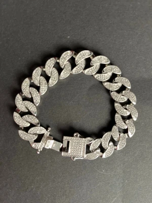 Silverfärgat glittrigt armband - Säljer ett chunky armband i silverfärg med stora länkar täckta av glittrande stenar. Armbandet har ett robust lås och ger en riktigt cool och trendig vibe. Perfekt för dig som vill sticka ut med accessoarerna!