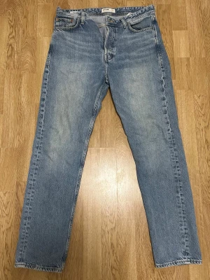 Blå raka jeans i vintage-stil - Ett par klassiska blå jeans med rak passform och vintage vibe. Jeansen har fem fickor, normal midja och subtila slitningar framtill för en avslappnad look. Tillverkade i slitstarkt denimtyg som passar perfekt till en casual outfit.