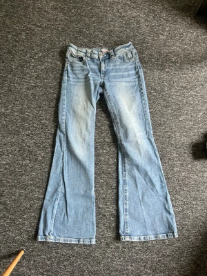 Ljusblå utsvängda jeans - Säljer ett par ljusblå jeans med utsvängda ben och klassisk femficksmodell. Jeansen har en snygg tvätt med slitningar och normalhög midja. Perfekta för dig som gillar retrostil och vill ha ett par bekväma och trendiga jeans. Säljer pga sitter ej bra på mig☺️☺️