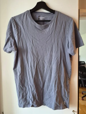 Blå t-shirt från Jack & Jones - En enkel blå t-shirt från Jack & Jones Essentials, tillverkad i mjuk ekologisk bomull. Klassisk rund halsringning och korta ärmar. Perfekt basplagg för alla tillfällen.