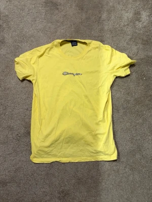 Gul t-shirt från Champion - Snygg gul t-shirt från Champion med klassisk logga broderad på bröstet. Tillverkad i mjuk bomull och har korta ärmar samt rund halsringning. Perfekt för en avslappnad och trendig stil.